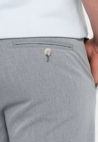 Harmaat muotilöydet, joissa on sileä pinta, varustettuna takataskulla, joka on koristeltu beigellä napilla ja hienovaraisella ommeltyylillä.