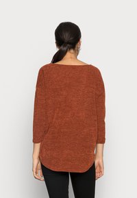 Pleteni svetr v rezavé barvě s tříčtvrtečními rukávy, širokým výstřihem a zaobleným lemováním. Texturovaná látka s volným střihem.