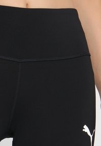 Černé sportovní legíny s vysokým pasem. Vyrobené z hladké, pružné tkaniny s bílým logem na spodní straně.