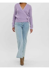 Lawendowy sweter z prążkowanej dzianiny, zapinany z przodu, z długimi rękawami, w połączeniu z jasnoniebieskimi dzwonami i brązowymi botkami za kostkę.