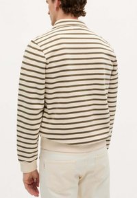 Pulover rayat în crem și maro, cu guler, mâneci lungi și un tiv ribbed. Material moale dintr-un amestec de bumbac, cu un finisaj texturat.