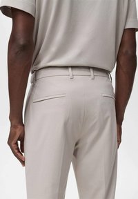 Pantalones de vestir de color beige claro con bolsillos en las costuras traseras, diseño de frente plano y textura de tela suave; combinados con una blusa gris de manga corta.