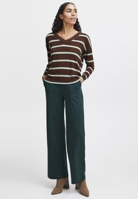 Pull en v marron et menthe à rayures avec des manches longues, associé à un pantalon large vert foncé et des chaussures à talons carré beige.