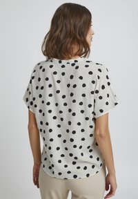 Blusa manica corta in crema chiaro con grandi pois neri. Presenta una vestibilità rilassata e un tessuto morbido e testurizzato. Orlo arrotondato.