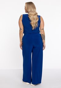 Kongeblå jumpsuit med ærmeløs design, bred ben-silhuet og blødt stof. Har en indsnøret talje og en flydende tekstur.
