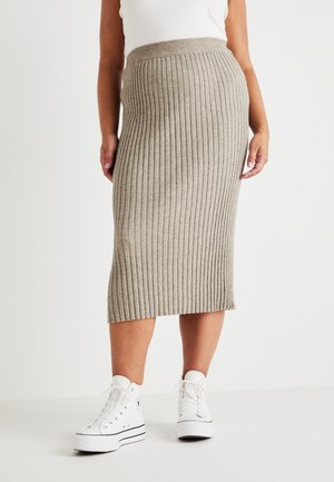 Jupe midi en tricot de couleur beige clair, avec une texture à côtes verticales, une taille ajustée, portée avec des baskets montantes blanches.