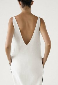 Hvid linne kjole med dyb V-udskærning, ærmeløs design og sidelommer, der har en simpel og ren silhuet.