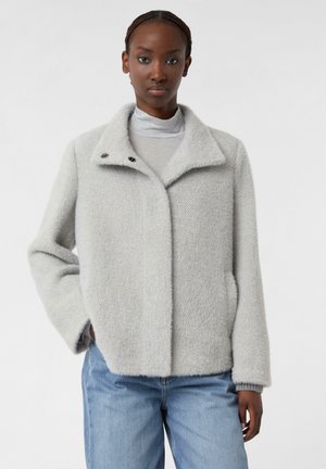 Light gray textured jacket with a collar, two buttons on the neckline, and side pockets, paired with a gray top and blue jeans.