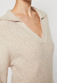 Beige stickad tröja med V-hals och bred krage, med en texturerad finish och avslappnad passform. Mjuk, lättviktig material.