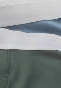 Trzy pary dopasowanego bielizny z elastycznymi białymi paskami w talii, wykonane z jasnoniebieskiego, ciemnoniebieskiego i oliwkowo-zielonego materiału. Teksturowany wzór paska.