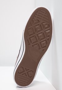 Hnědá gumová podrážka boty s geometrickým vzorem, se bílým bočním pruhem a logem "Converse All Star."