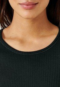 Top nero a costine con scollatura tonda, caratterizzato da una superficie liscia e un leggero elastico. Ingrandimento dei dettagli del tessuto e della scollatura.
