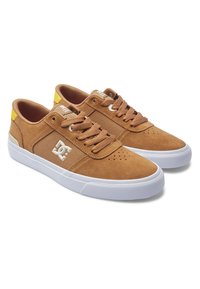 Brune ruskindssneakers med hvid gummisål, snøredesign, perforeret tåboks, side-logo og en gul detalje ved hælen.