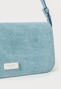 Light blue denim crossbody bag with a smooth texture, silver logo plate, and contrasting stitching. Adjustable strap for versatility.