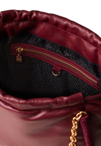 Burgundy leather bag with a soft, gathered top. Features a black textured lining and a gold zipper pocket with a decorative pull.