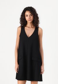 Robe noire sans manches avec un décolleté en V, coupe décontractée et deux poches avant. Fabriquée en tissu lisse avec un design minimaliste.
