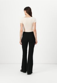 Top aderente color beige chiaro con maniche corte, abbinato a pantaloni neri a vita alta e svasati. Tessuto liscio, design minimalista, senza motivi visibili.