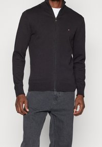 Grafitowy sweter rozpinany na zamek, wykonany z dzianiny, z wysokim kołnierzem, długimi rękawami i małym logo na lewej piersi.