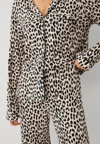 Leopardskindet pyjamasæt lavet af letvægtsstof. Har sorte detaljer, lange ærmer og en knaplukning med en brystlomme.