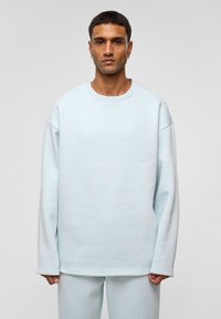 Lichtblauwe oversized sweatshirt gemaakt van zachte stof, met een ronde halslijn en verlaagde schouders, voorzien van een eenvoudige, gladde textuur.