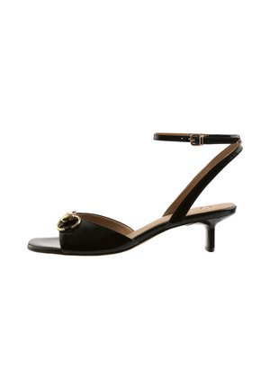 Czarna sandałka z lakierowanej skóry z odkrytymi palcami, niskim obcasem typu kitten heel, paskiem na kostce z klamrą oraz złotym łańcuszkiem na przednim pasku.