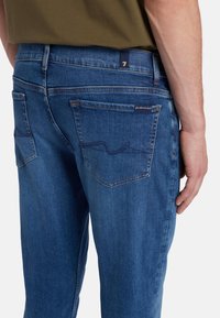 Jeans in denim blu scuro con vestibilità dritta, dotati di due tasche posteriori e dettagli di cucitura discreti. Il tessuto ha una texture liscia.