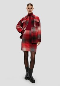 Czerwona, w kratę, oversize'owa kurtka z dwiema kieszeniami na piersi, w połączeniu z pasującą, sięgającą do kolan spódnicą. Całość dopełniają czarne botki za kostkę.
