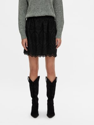Black eyelet skirt with scalloped hem, textured design; paired with knee-high black suede boots featuring decorative stitching and pointed toes.