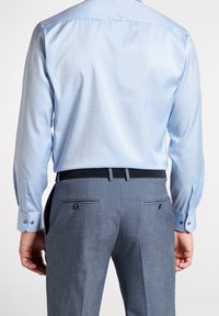 Ljust blå skjorta med en slät, glänsande yta, i kombination med grå, strukturerade byxor som har två bakfickor och ett svart bälte.