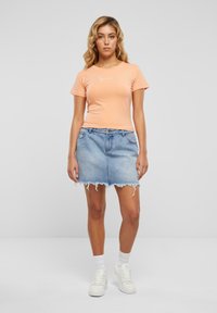 Ferskenfarget kortermet tettsittende T-skjorte med hvit skrift, sammen med en lyseblå denimskjørt med frynset kant. Hvite joggesko og sokker.
