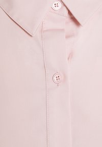Light pink button-up shirt collar and placket with stitched seams and two visible round buttons.