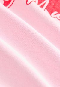 Detailný záber na mäkkú ružovú tkaninu s čiastočne viditeľným červeno-bielym potlačeným vzorom hore.