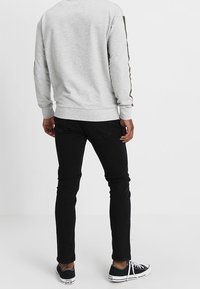 Sudadera gris de manga larga con puños y dobladillo acanalados, combinada con jeans negros ajustados y zapatillas náuticas azul marino. Franjas laterales en la sudadera.