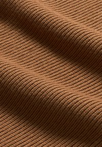 Nahaufnahme eines weichen, gerippten braunen Stoffes mit sichtbarer Textur und sanften Falten, die Schatten erzeugen.
