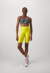 Sujeción deportiva en gris con tirantes ajustables y detalle del logo, combinada con pantalones cortos de ciclista en un brillante color amarillo, ambos hechos de un tejido elástico y que absorbe la humedad.