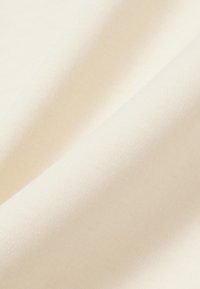 Tissu en coton de couleur crème douce, présentant un tissage texturé subtil, légèrement drapé pour mettre en valeur sa finition lisse et sa légère réflectivité.