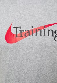 Szary bawełnowy t-shirt z dużym czerwonym logo w kształcie łuku oraz czarnym napisem "Training" na przodzie.