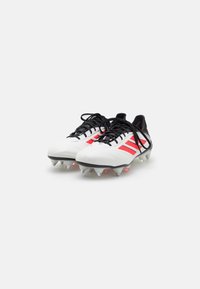 White soccer cleats with black laces and three red stripes. Textured upper, black sole with clear studs, and a rounded toe design.