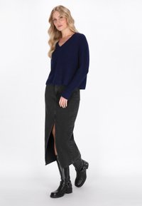 Granatowy sweter z dekoltem w serek, czarna spódnica dżinsowa z przednim rozcięciem i czarne botki za kolano z klamrami.