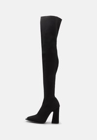 Zwarte over-de-knie laarzen gemaakt van ribbelstof, met een puntige neus en een stevige hoge hak voor stabiliteit.