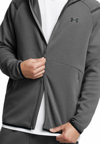 Gray zip-up hoodie with black accents, made from soft fabric. Features two side pockets and a white inner layer visible at the bottom.