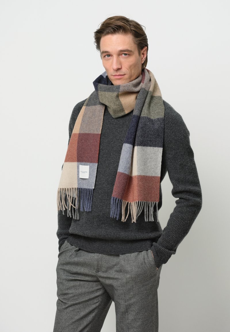 Écharpe en laine avec un motif à carreaux dans des nuances de gris, marron et bleu marine, avec des franges aux extrémités et une étiquette de marque dans le coin.
