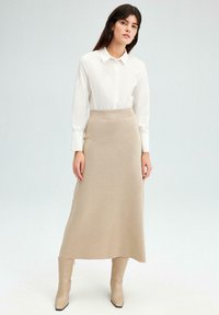 Fustă midi tricotată bej cu un elastic la talie, asociată cu o cămașă albă cu nasturi. Textură netedă, de culoare deschisă și design ajustat.