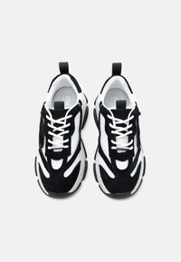 Ζευγάρι αθλητικά παπούτσια σε μαύρο και άσπρο με χοντρές σόλες και λευκά κορδόνια, σε θέα από πάνω σε λευκό φόντο.