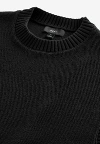 Schwarzer Strickpullover mit einem gerippten Rundhalsausschnitt, der eine strukturierte Oberfläche aufweist und ein Etikett mit der Aufschrift "NEXT" hat. In mittlerer Größe erhältlich.