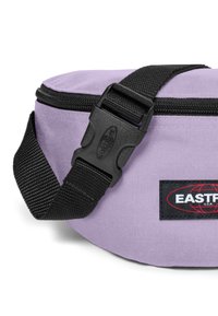 Levandulová látková ledvinka s černým nastavitelným popruhem, bočním uvolňovacím sponou, zipovým uzávěrem a odznakem s logem "EASTPAK U.S.A.".