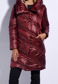 Manteau rembourré bordeaux avec un large col, un design en diagonale de piquage et des poches latérales. Texture brillante et accents en métal doré.