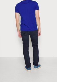 Camiseta de algodón azul con mangas cortas, combinada con vaqueros oscuros y zapatillas estampadas con diseño en azul y negro.