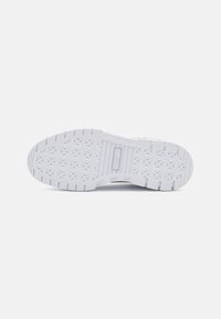 Suela de una zapatilla con un material de goma blanca texturizada que presenta patrones geométricos y un logo incrustado cerca del área del talón.