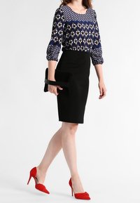 Gonna a matita nera abbinata a una blusa a fantasia blu navy con maniche a tre quarti, completata da tacchi a spillo rossi e una pochette nera.